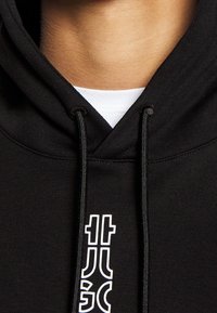 Sort hættetrøje med snørebånd og hvidt logo detaljeret på fronten, lavet af glat, tykt stof med en hyggelig tekstur.