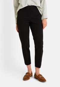 Pantalones ajustados negros con una textura suave, piernas ajustadas y una cintura de altura media, combinados con mocasines marrones con un acento dorado.