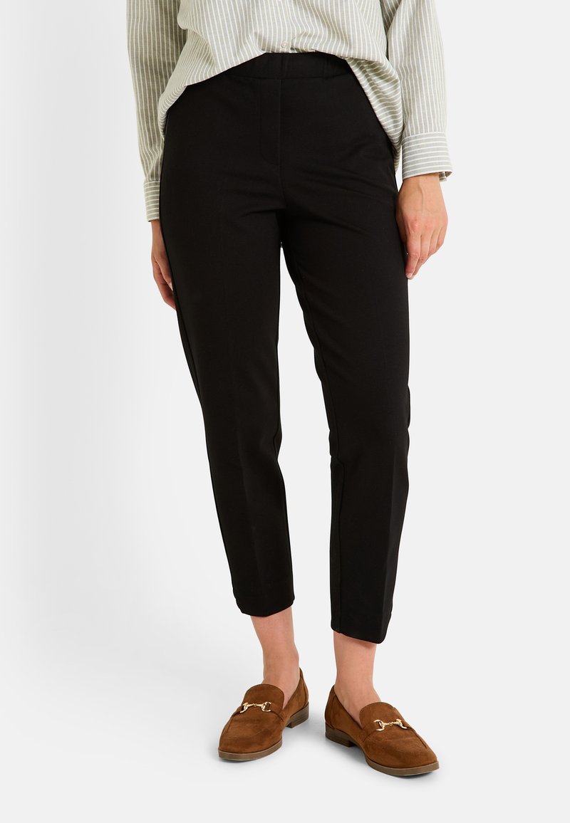 Pantalones ajustados negros con una textura suave, piernas ajustadas y una cintura de altura media, combinados con mocasines marrones con un acento dorado.