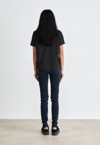 Black short-sleeve t-shirt, fitted jeans, and platform shoes. Smooth texture; simple design. Hair falls straight back. Plain background.