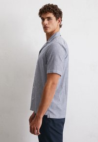 Short-sleeve button-up shirt in blue with white vertical stripes; features a camp collar and a relaxed fit. Fabric appears lightweight.