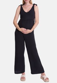 Schwarzer Jumpsuit mit Rundhalsausschnitt, gebundenen Schulterträgern und weit geschnittenen Beinen. Hergestellt aus strukturiertem Stoff, mit versteckten Reißverschlüssen.