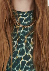 Collar de cadena de oro con diseño entrelazado, usado sobre un suéter texturizado de leopardo verde que presenta acentos en amarillo y blanco.