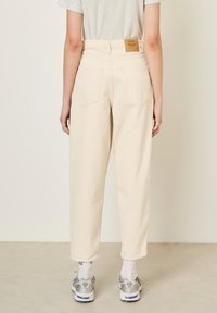 Pantalons en denim crème à coupe décontractée, avec un design à cinq poches, des coutures visibles et une étiquette cousue à la taille à l'arrière.