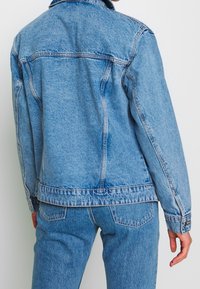 Světle modrá džínová bunda s klasickým designem, vybavená bočními kapsami a manžetami na knoflíky. Nositelná s odpovídajícími světle modrými džínami.