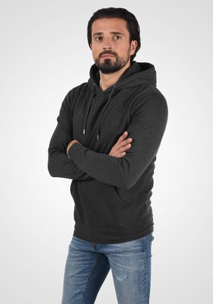 Sudadera con capucha de color carbón, de manga larga, con bolsillo frontal y cordones; combinada con unos pantalones vaqueros de mezclilla azul claro desgastados.