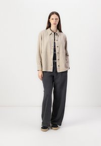 Lys beige knappjakke med krage og frontlommer, kombinert med mørkegrå vide bukser og svarte sko med beige såler.