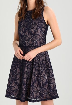 Marineblaues ärmelloses Kleid mit enganliegendem Oberteil und schwingendem Rock. Mit einer floralen Spitze überzogen, die zarte Stickereien und einen gewellten Saum aufweist.