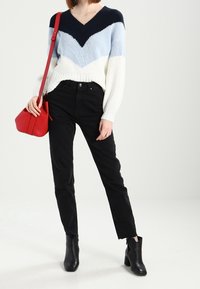 Objemný pletený svetr s vzorem do cik-cak v námořnické modré, světle modré a bílé. V kombinaci s černými džínami s vysokým pasem a černými kotníkovými botami. Červená crossbody taška.