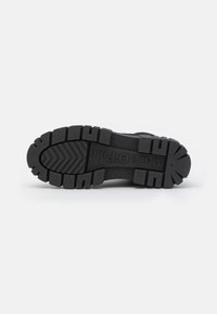 Semelle de chaussure noire avec des crampons profonds et la marque "Marc O’Polo" embossée au-dessous, présentée sur un fond clair uni.