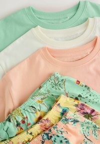 Trois sweat-shirts pastel en vert menthe, crème et pêche empilés au-dessus de trois paires de shorts à motifs floraux en vert menthe, jaune et multicolore.