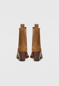 Cizme de gleznă din suede maro, cu un toc bloc de înălțime medie și un tab de rătărspate. Panourile laterale netede îmbunătățesc designul aerodinamic.