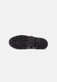 Semelle en caoutchouc noir avec un motif texturé, dotée de profondeurs et de crampons pour une adhérence optimale. Conçue pour résister et offrir une bonne prise sur différentes surfaces.