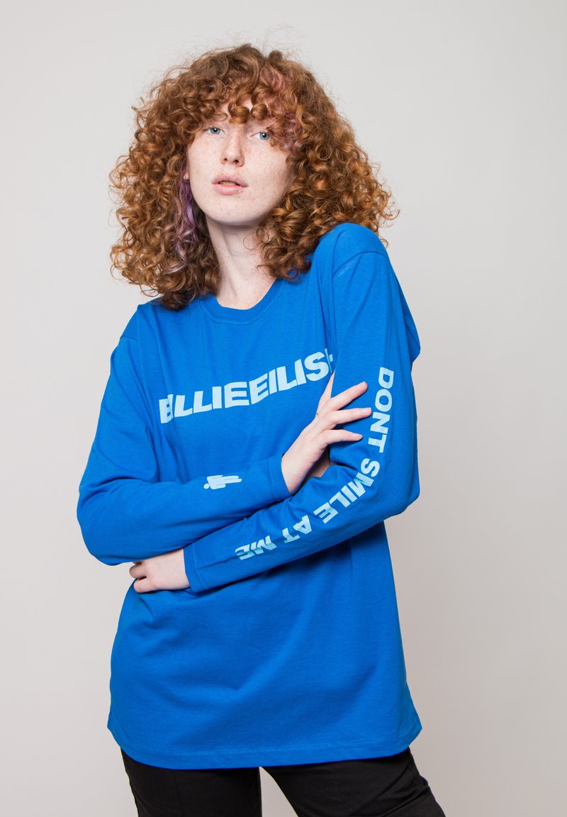 Long-sleeve blue cotton t-shirt featuring bold white text on the front and sleeve reading "BILLIE EILISH" and "DON'T SMILE AT ME."