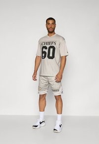 Conjunto atlético cinzento com uma camisola de manga curta com "CHIEFS" e o número 60 impressos a preto, combinado com calções às riscas correspondentes e ténis brancos.