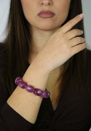 Pulsera de cuentas moradas en una muñeca, con cuentas lisas y brillantes de diversas formas, acentuadas con pequeños separadores dorados.