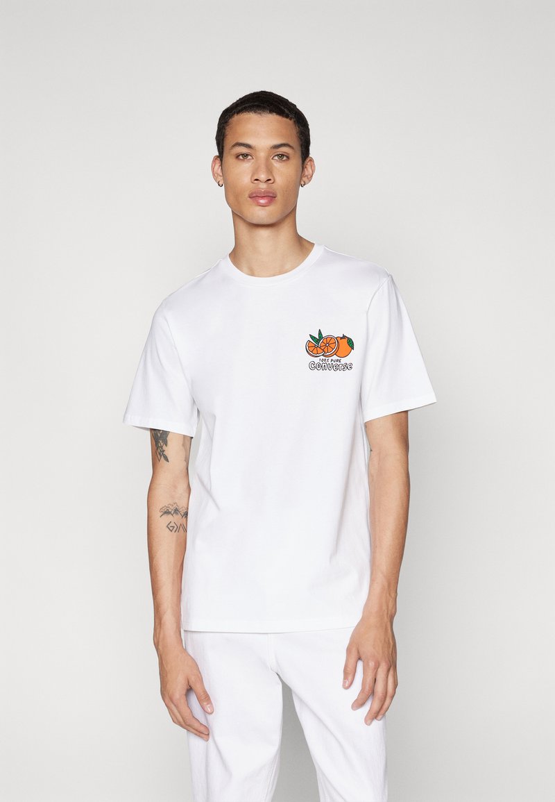 Camiseta blanca de algodón con un gráfico de fruta naranja y texto en el lado izquierdo del pecho. Mangas cortas, escote redondo y corte relajado.