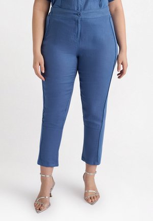 Pantalones de mezcla de lino azules con una textura suave, corte entallado y detalles en las costuras laterales, combinados con unos zapatos de tacón plateados con tiras.