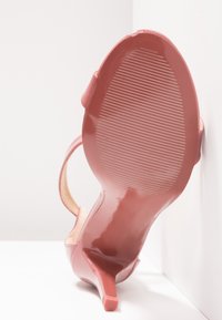 Chaussure à talon haut rose posée sur le côté montrant la semelle rainurée et le talon fin sur fond blanc.