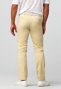 Beige katoenen broeken met een rechte pasvorm, voorzien van achterzakken met knopen en een eenvoudig ontwerp. Gecombineerd met witte sneakers.