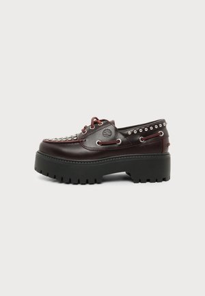 Mørke burgunderfargede skinnplattform loafers med tykk svart grovmønstret såle, metallnitter, snøredetaljer og preget merke-logo på siden.