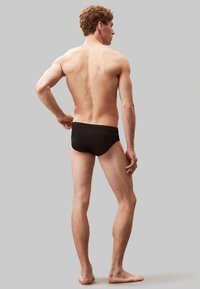 Bañadores negros de corte ajustado, fabricados en una tela suave, con un diseño de cintura baja, estilo minimalista y sin patrones ni adornos visibles.