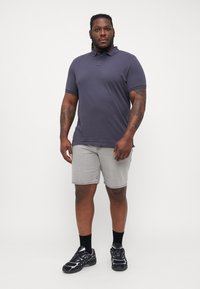 Korte erm polo i marineblå, kombinert med lysegrå denimshorts og sorte joggesko. Har krage og treknaps lukking.