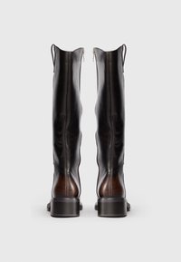 Egy pár magas, barna bőrcipő hátsó cipzárral, húzófülekkel és alacsony, blokksarkú talppal, fehér háttér előtt.