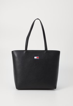 Czarna skórzana torba typu tote z dwoma długimi uchwytami i małą prostokątną naszywką z logo w kolorach czerwonym, białym i niebieskim na środku przodu.