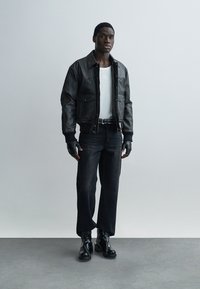 Μαύρο δερμάτινο μπουφάν bomber, λευκό μπλουζάκι, σκούρο τζιν, μαύρα γάντια και μποτάκια με φερμουάρ. Μινιμαλιστικός σχεδιασμός και μονόχρωμα χρώματα.