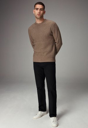 Pull côtelé beige, pantalon noir et baskets blanches. La coupe est décontractée, avec un col rond et un tissu texturé. Design minimaliste.