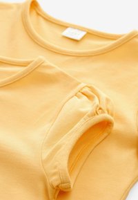 Deux t-shirts en coton jaune avec des encolures rondes, une texture douce et des détails de manches froncées, présentés se chevauchant sur un fond blanc.