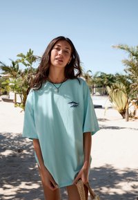 Jasnoniebieska, oversize koszulka bawełniana z małym haftowanym wzorem ryby. Krótkie rękawy i luźny krój o miękkiej fakturze.