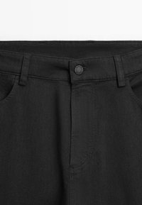 Black denim pants featuring a button closure, front pockets, and a textured fabric with a slight sheen.
