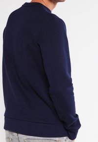 Sweat-shirt bleu marine en tissu doux, avec col rond et manches longues, bordures côtelées aux poignets et à l'ourlet, avec un style minimaliste.