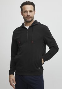 Crna zip-up dukserica od mekanog materijala, s prednjim džepom, crvenim detaljima na zipu i uskim krojem. Jednostavna, u jednoj boji bez uzoraka.