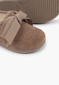 Scarpe in suede marrone con un grande fiocco coordinato sulla parte anteriore, perforazioni decorative e una suola in gomma testurizzata per una migliore aderenza.