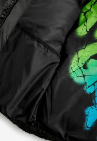 Veste rembourrée noire avec un motif de peinture en spray abstrait vibrant vert et bleu, texture lisse et bord élastique à l'ourlet et aux poignets.