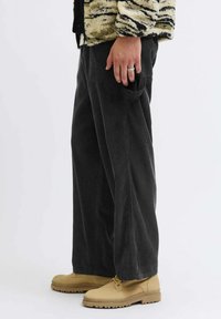 Sive široke hlače od kordura s bočnim džepovima, uparene s bež cipelama na vezivanje. Tekstura je rebrasta s mekim završetkom.