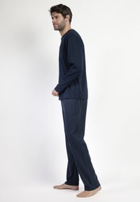 Topp de manga larga azul marino con un bolsillo texturizado y pantalones de pijama a rayas a juego. Los materiales parecen suaves, ligeros y adecuados para ropa de estar en casa.