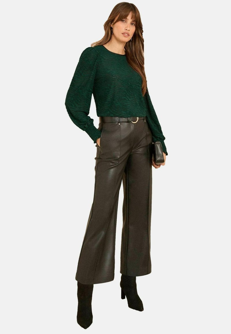 Maglione lavorato a maglia verde scuro con maniche lunghe, abbinato a pantaloni larghi in faux pelle nera a vita alta e stivali neri con punta.