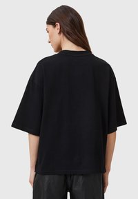 Camiseta negra de gran tamaño hecha de algodón, con mangas cortas y cuello redondo. La tela tiene una textura suave y detalles de costura mínimos.