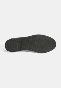 Zwarte rubberen schoenzool met een gestructureerd oppervlak en gelijkmatig verdeelde, verhoogde stippen voor grip, ronde neus en platte hak.