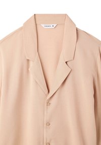 Camicia beige con colletto, dalla texture liscia, con chiusura a bottoni e cinque bottoni. L'etichetta riporta "TERRANOVA" e taglia "S."