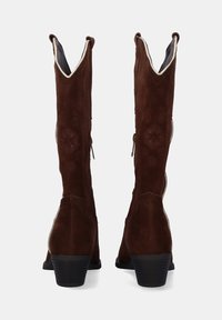 Botas altas de ante marrón con un patrón texturizado, parte superior en ángulo y cremalleras en la parte trasera. Cuentan con un tacón bloque para mayor estabilidad.
