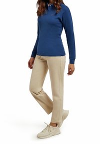 Niebieska koszula polo z długim rękawem z kołnierzykiem, zestawiona z beżowymi spodniami o prostym kroju i jasnymi sneakery. Casualowy strój na modelce.