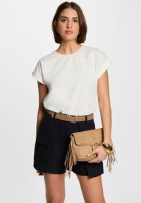 White short-sleeve blouse with floral embroidery, paired with dark blue tailored shorts and a tan fringed crossbody bag.