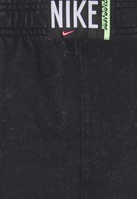 Svarta bomullsshorts med elastisk midja, Nike-logga i vitt med rosa accent och kontrasterande "Just Do It"-etikett i grönt.