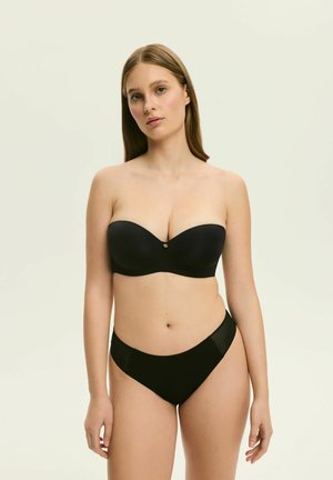 Czarny stanik bez ramiączek z gładkiego materiału, formowanymi miseczkami i małym metalowym akcentem. W połączeniu z dopasowanymi czarnymi majtkami typu bikini o niskim stanie.
