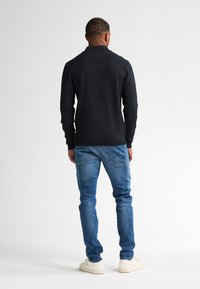 Maglione di lana nera con maniche lunghe, abbinato a jeans in denim blu e sneakers bianche. Cuciture visibili e motivo a maglia testurizzato.